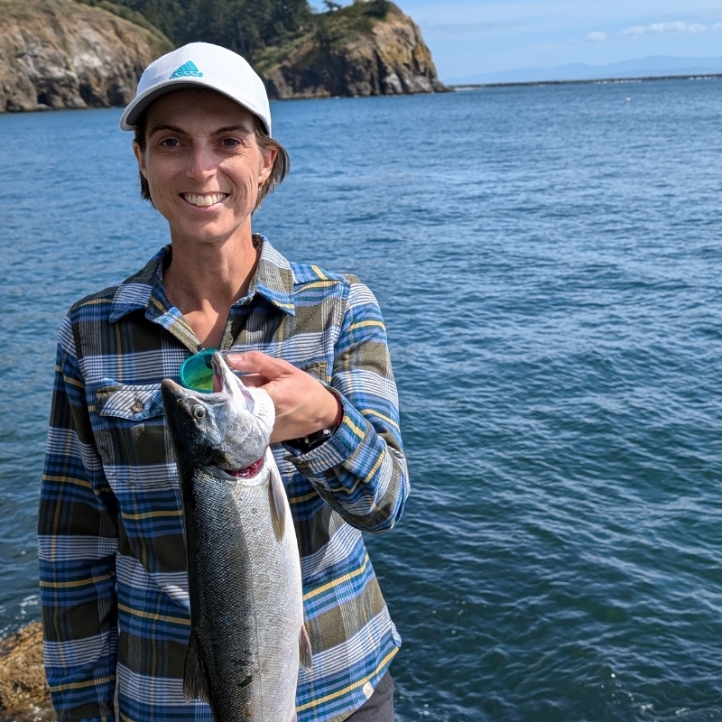 Amber Hanson holding a fish in hand while smiling at a lake.
