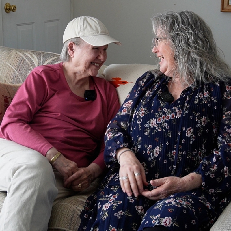 Kay Bradford and Deborah Taylor sitting on a couch talking to each other.