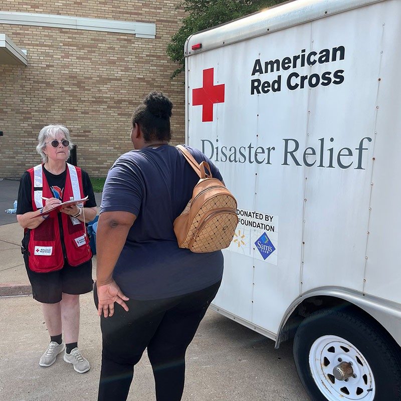 Red Cross volunteer speaking with resident next to a Red Cross Disaster Relief trailer.