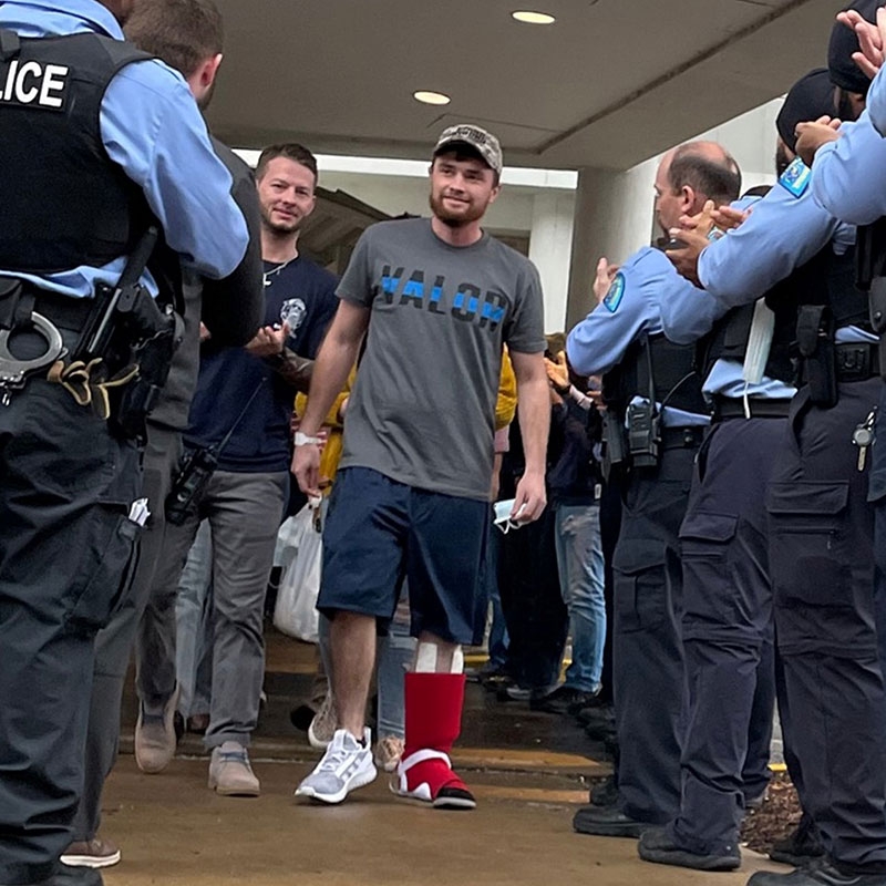 person with a cast on left leg, walks by a group of officers that are clapping.