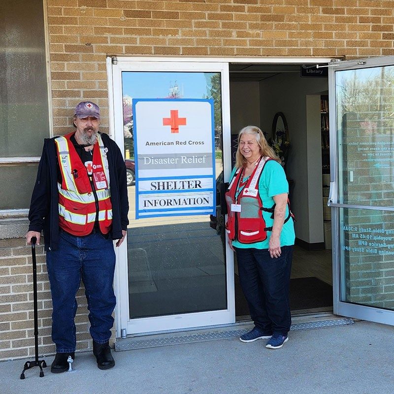 Red Cross volunteers Skip Cook and Sally Wilsey standing next to a door with a Red Cross logo on it.