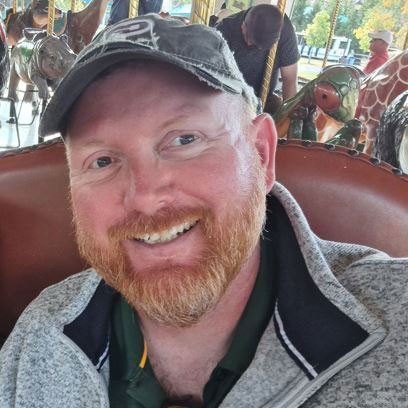 Angus Macaskill wearing jacket and hat takes a selfie while on a merry-go-round.