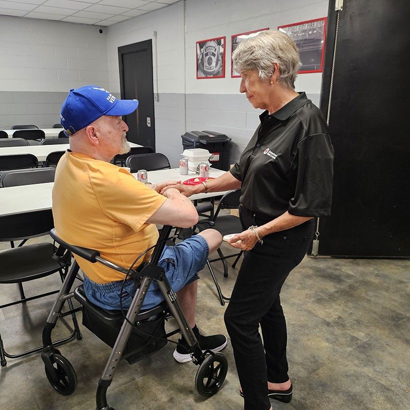 Red Cross volunteer comforting man sitting down on a walker.