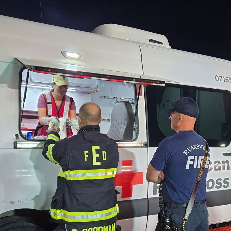 Red Cross volunteer serving food to fire fighters through a Red Cross van side window.
