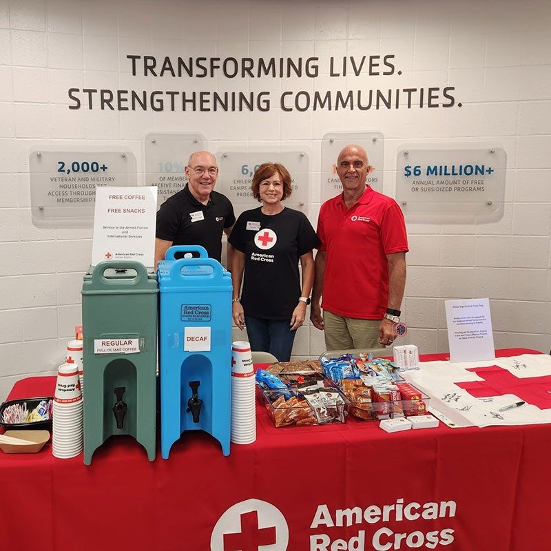 three members of the Service to the Armed Forces team standing next to a table with coffee and snacks.