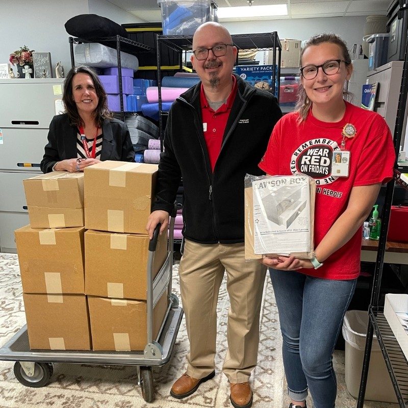 Three Red Cross volunteers standing next to stacks of boxes in a storage closet.