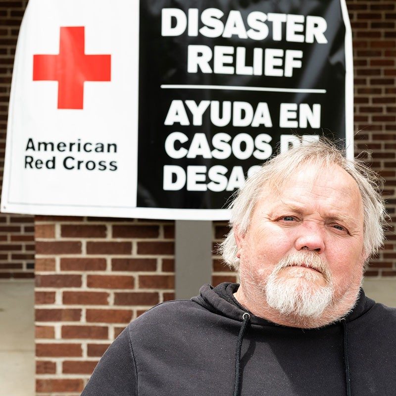 man next to a Red Cross disaster relief banner on a building.