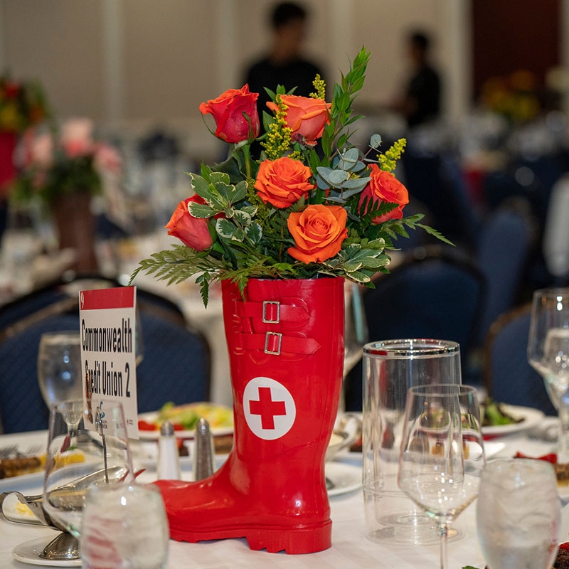 decorative boot with a red cross logo and flowers in the boot on a dinner table.