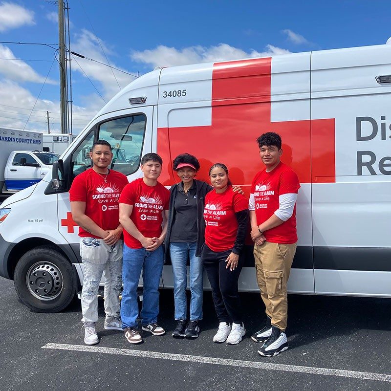 five Red Cross volunteers standing next to a Red Cross van in a parking lot.