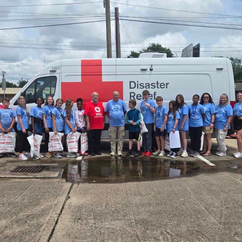 Group of children posing for a photo in front of a Red Cross Emergency Vehicle.