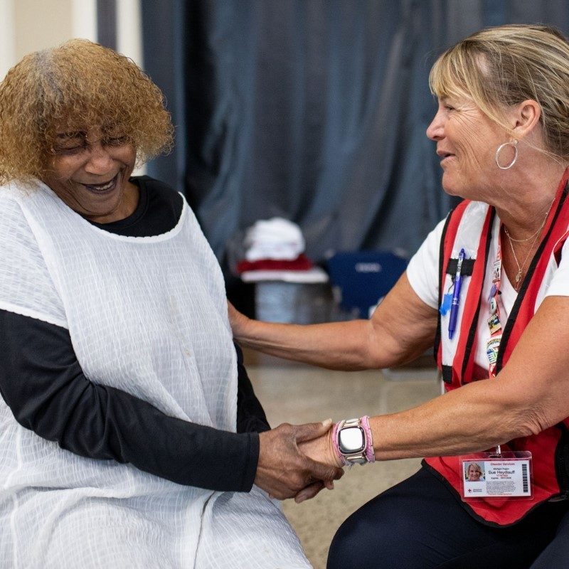 Red Cross volunteer holing hand of a client in a shelther. 