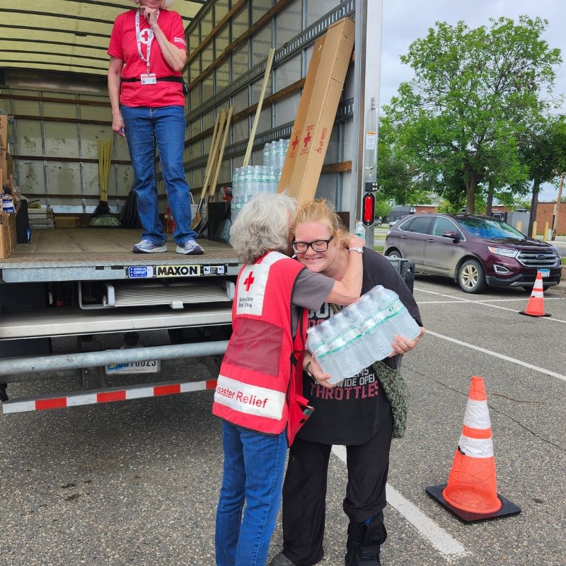 A Red Cross volunteer hugging a client with water in the client's hand. 