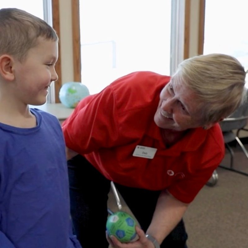 Deb Perkins with a ball in her hand talking to a small child 