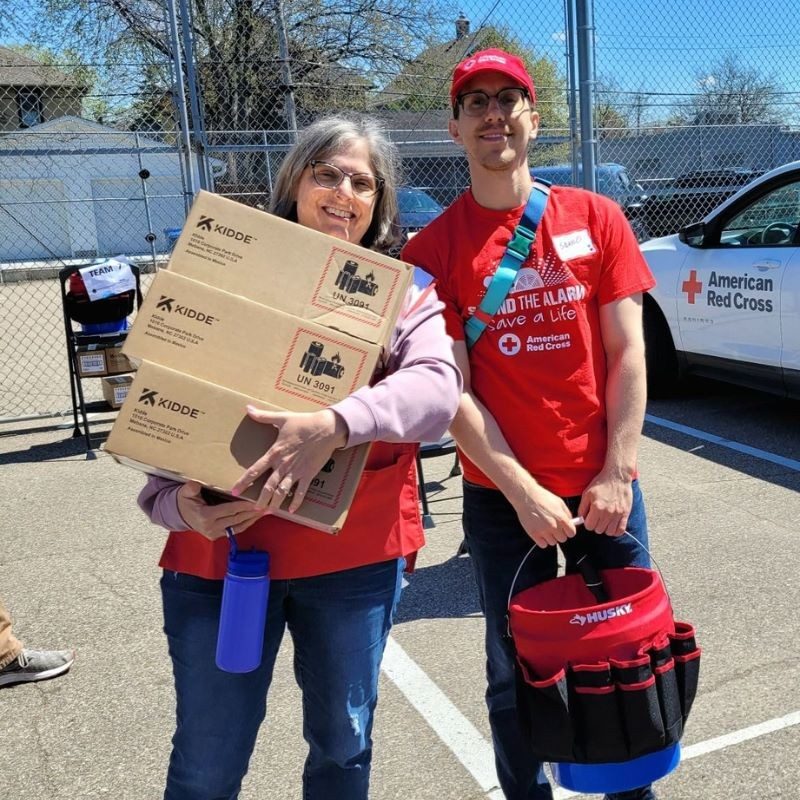 Two red cross volunteers holding supplies in their hands smiling