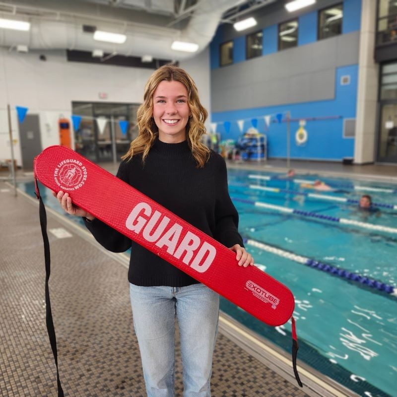 Amber holding a lifeguard flotation device smiling standing in front of a pool.