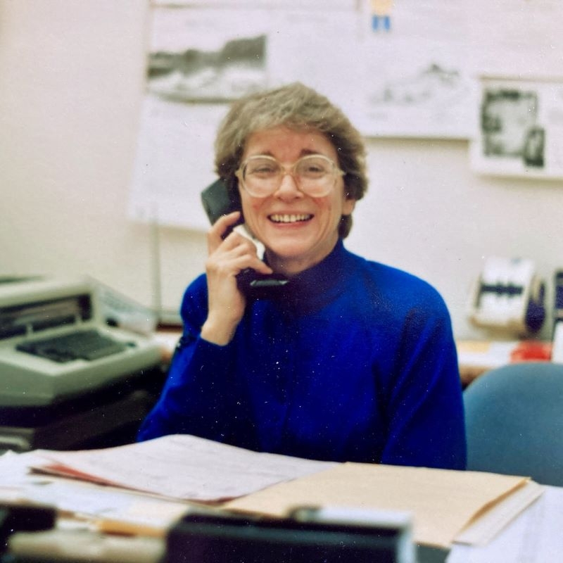 Peg on the phone at a desk smiling.