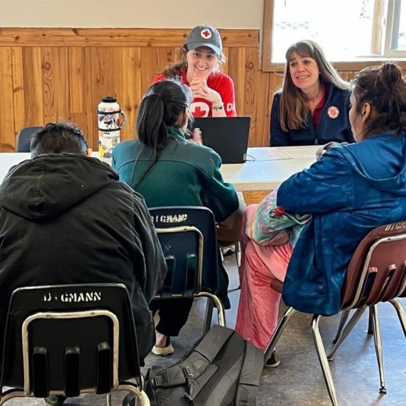Two Red Cross volunteers speaking with a famiy of three at a desk. 