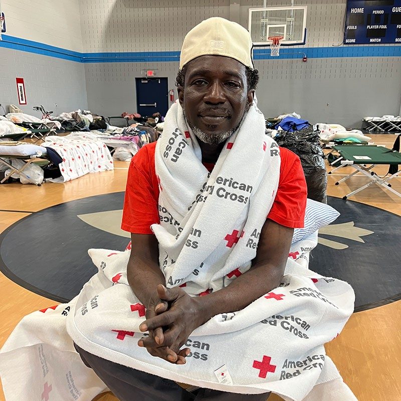 Steven Reason sitting in a Red Cross shelter with a Red Cross blanket wrapped around his shoulders.