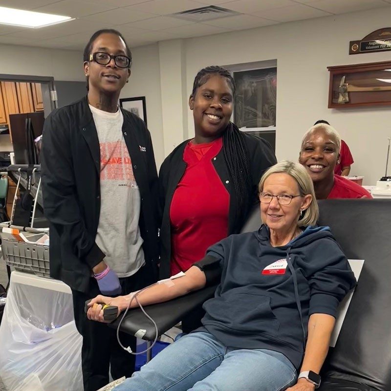 Jerene Kessler sitting in chair donating blood with Red Cross staff members next to her.