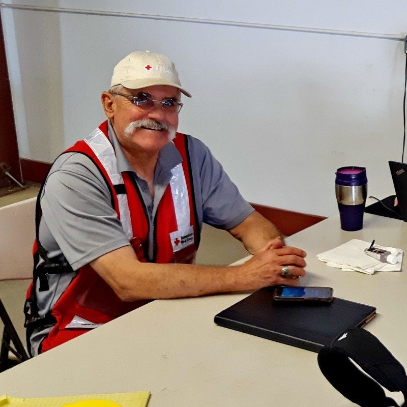 Will sitting at a deskin a Red Cross vest smiling.