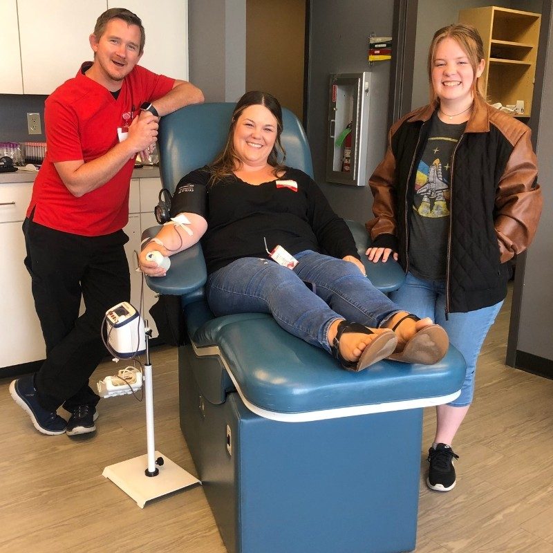 Two people standing next to a person donating blood.