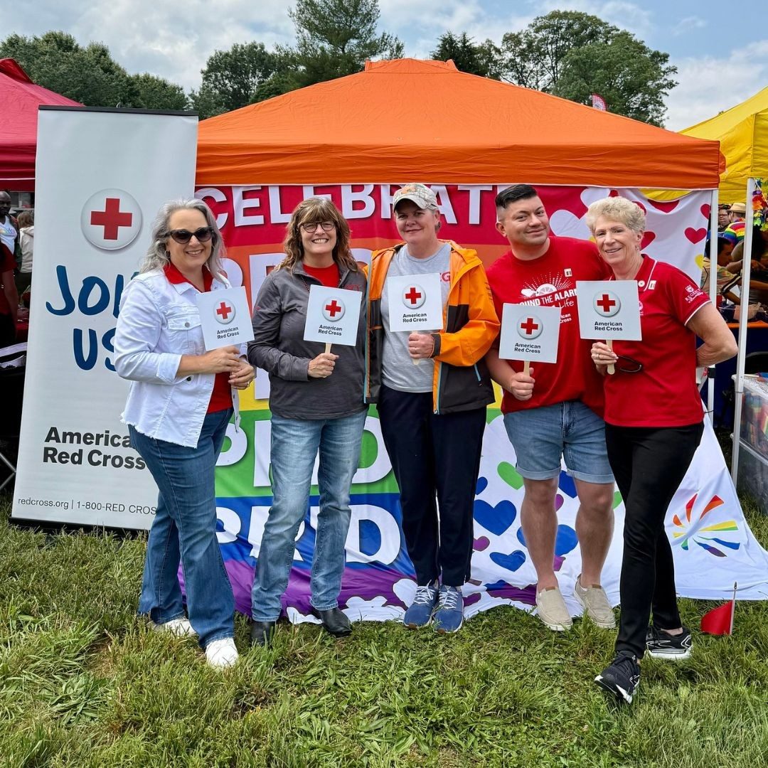 red crossers holding up red cross signs in front of pride tent
