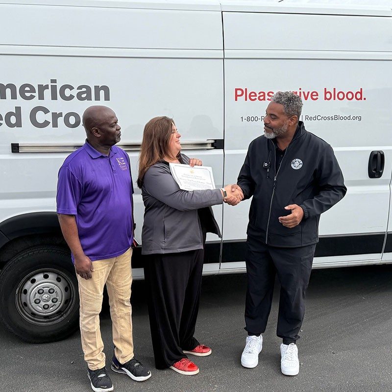 three people standing by a Red Cross van with two of them shaking hands.