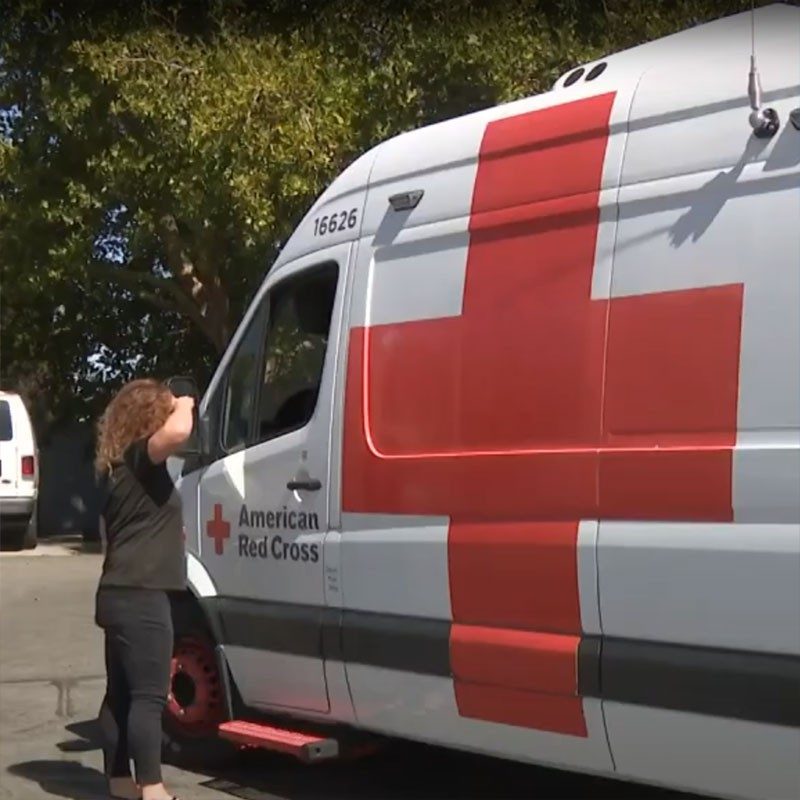 person standing next to the driver side window of a Red Cross van.