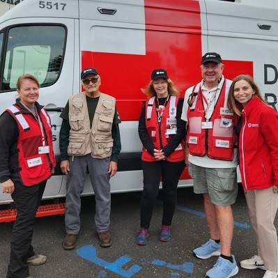 five Red Cross volunteers standing next to a Red Cross van in a parking lot.