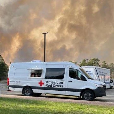 A Red Cross Disaster Relief van parked on the street with a large cloud of smoke in the background.