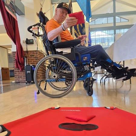 Veteran in a wheelchair playing cornhole bean bag toss.
