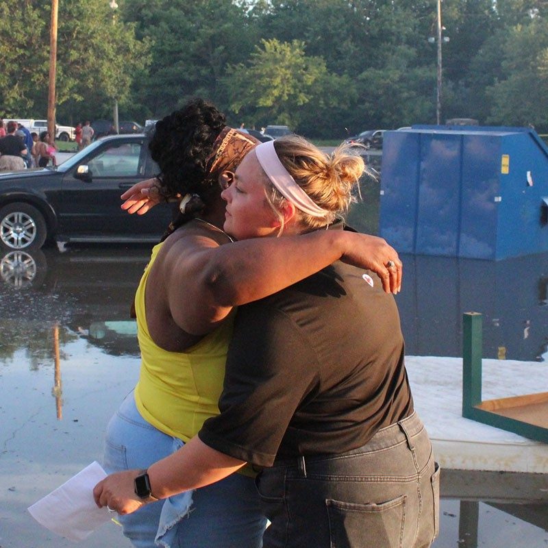 Red Cross volunteer hugging a another person, with flood waters all around.