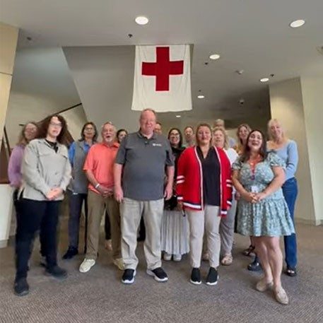group pic of Red Cross staff members with a large Red Cross flag hanging above their heads.