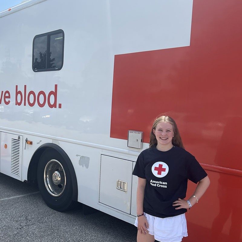 Red Cross volunteer Maddie Frank standing next to a Red Cross bloodmobile.