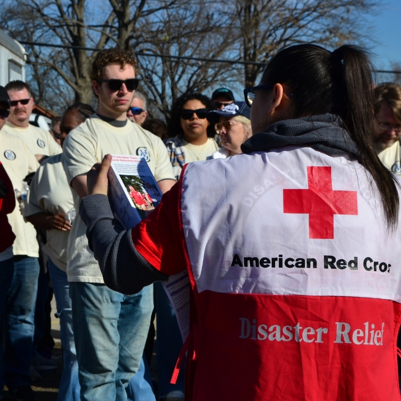 Red Cross volunteer in vest speaking to a crowd.
