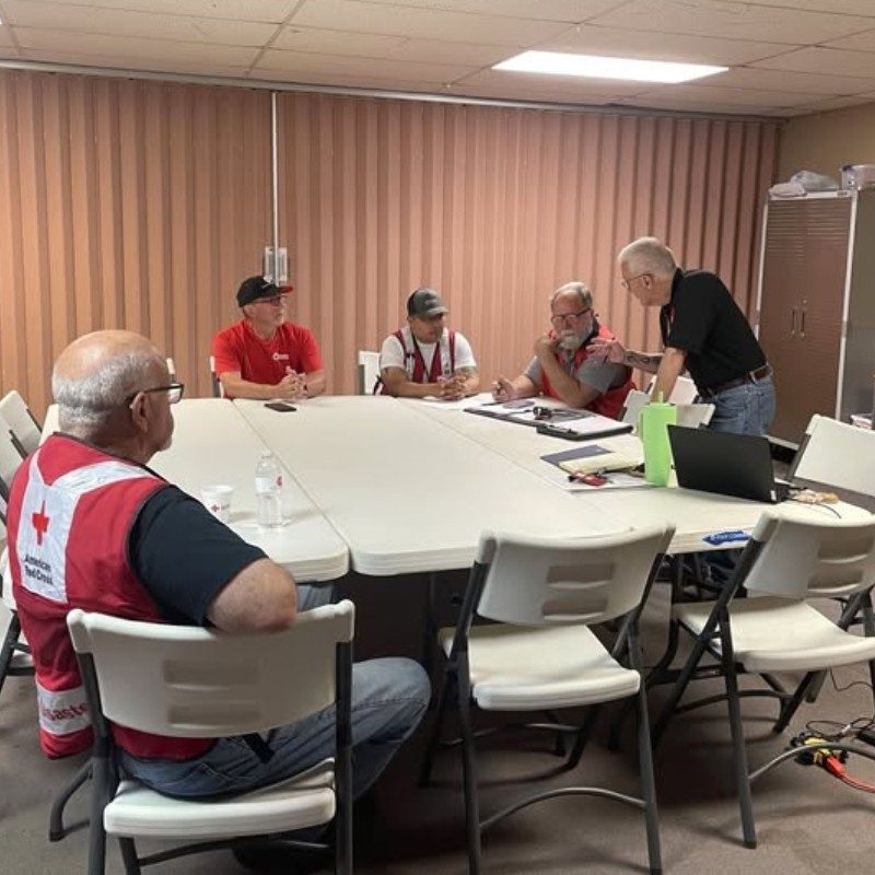 A group of Red Cross volunteers sitting around a table talking to each other.