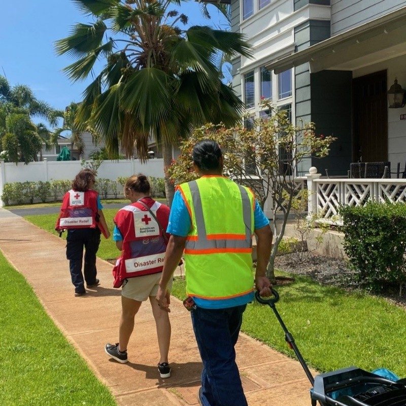 Three Red Cross volunteer wearing a red cross vest walking down street with supplies