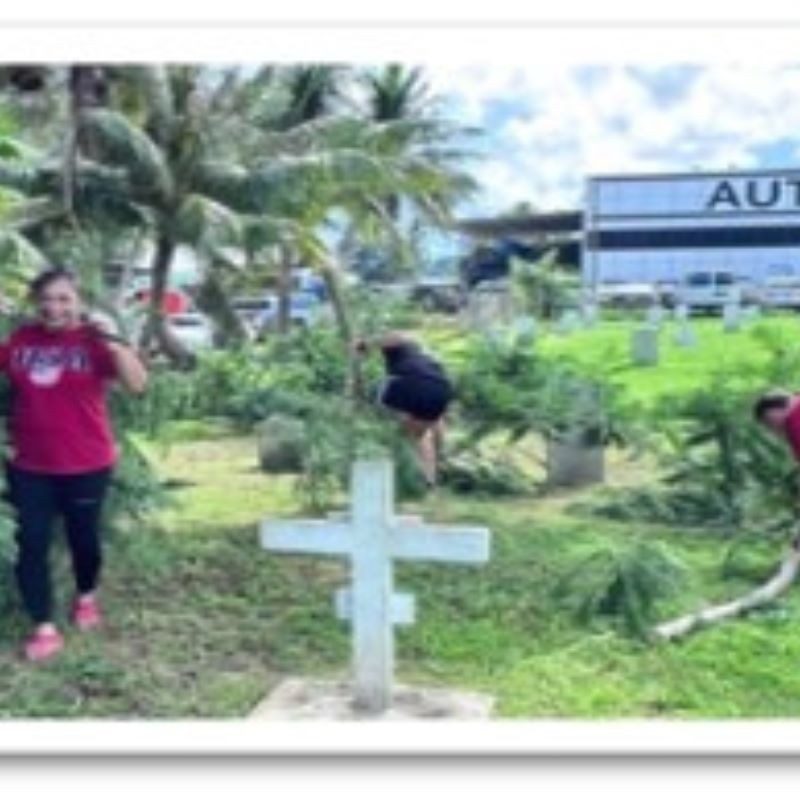 Volunteers cleaning up a burial ground with cross in the background.
