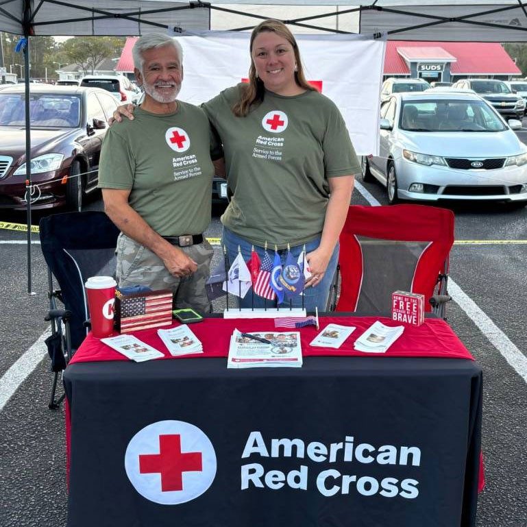 two Red Cross volunteers standing at a table with Red Cross pamphlets.