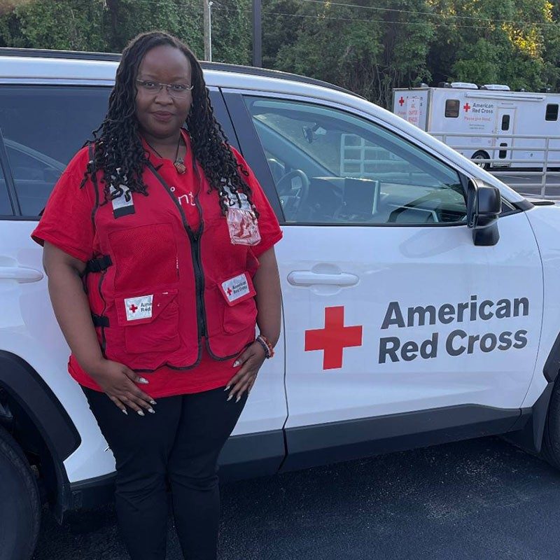 Red Cross volunteer Selenia Sadai wearing a Red Cross vest and standing next to a Red Cross vehicle.