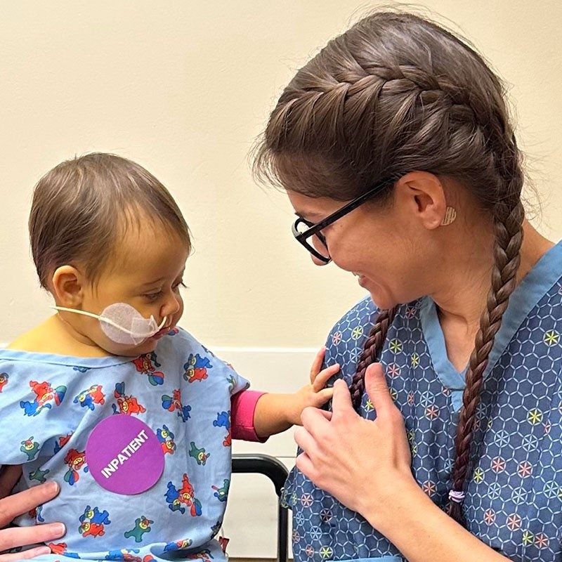 9-month-old girl, with tube in nose, touching the arm of blood donor Amanda Graham.