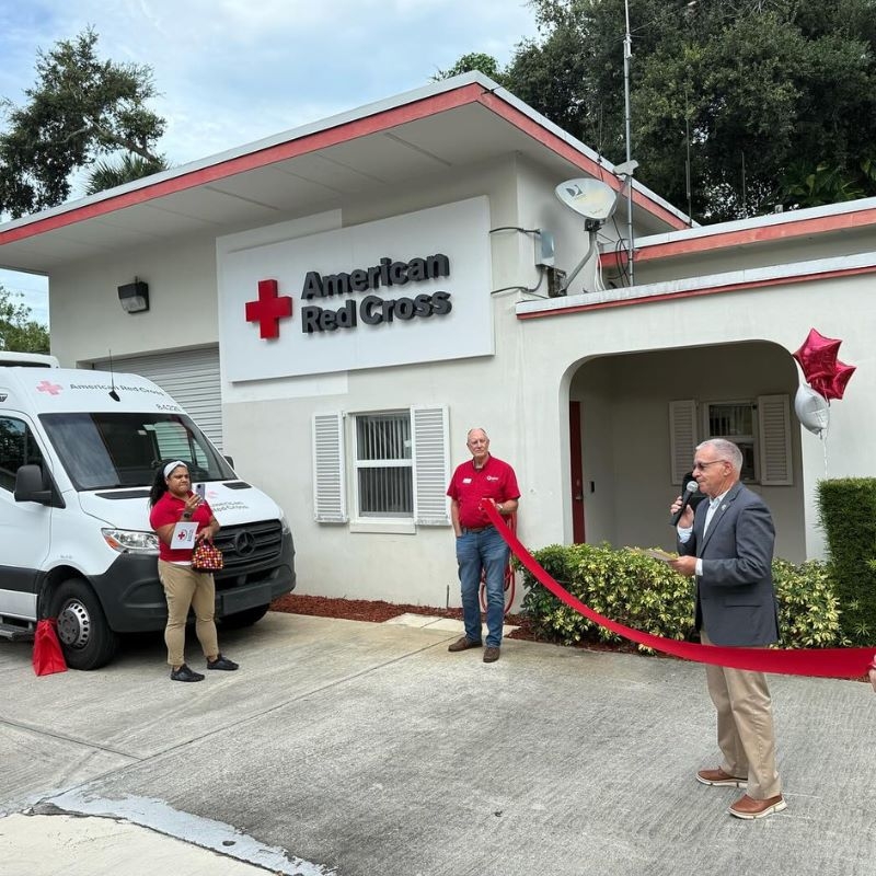 Two people holding a long ribbon in front of a building.