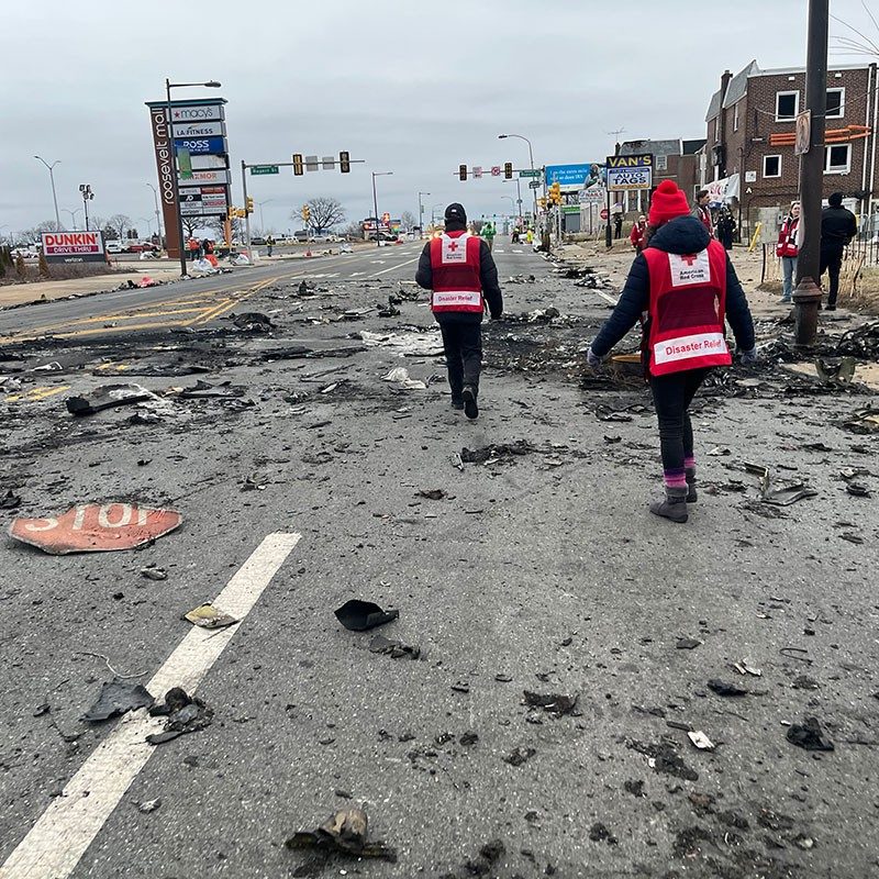 Red Cross volunteers walking down a street that has debris scattered all around.