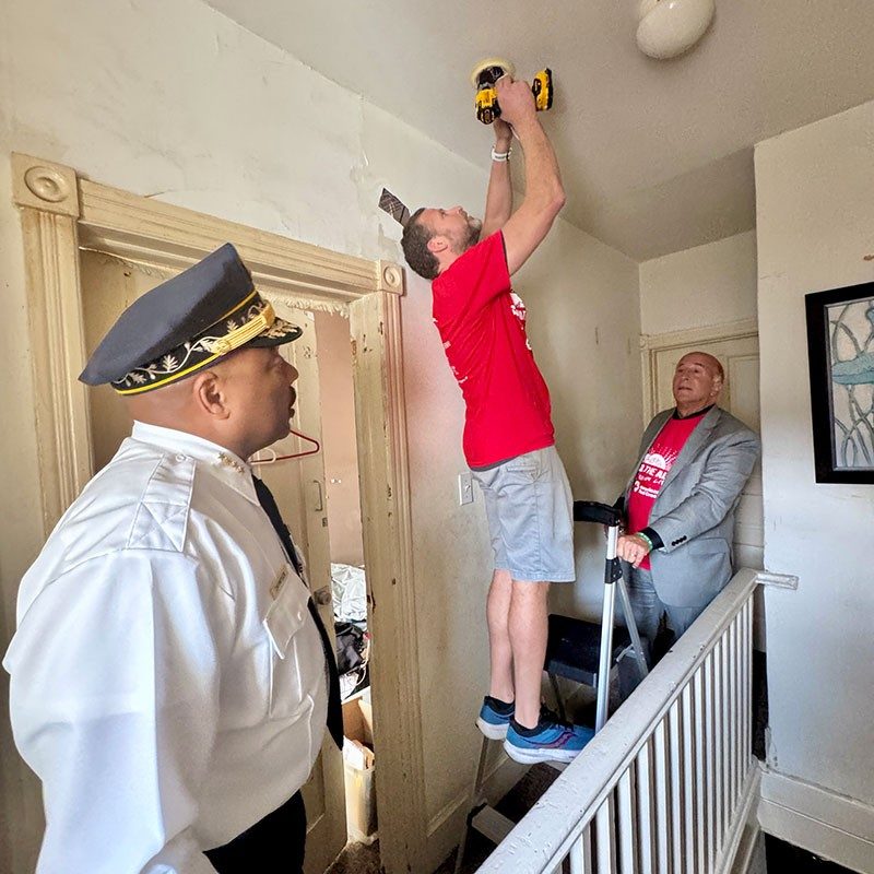 Red Cross volunteers installing a smoke alarm in a home with Philadelphia Fire Commissioner Jeffrey Thompson watching.