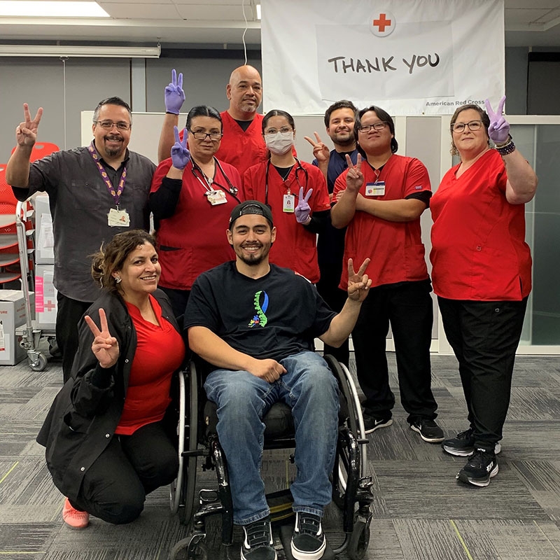 Mikie Guerrero in a wheelchair with Red Cross staff standing by him while giving the peace sign.