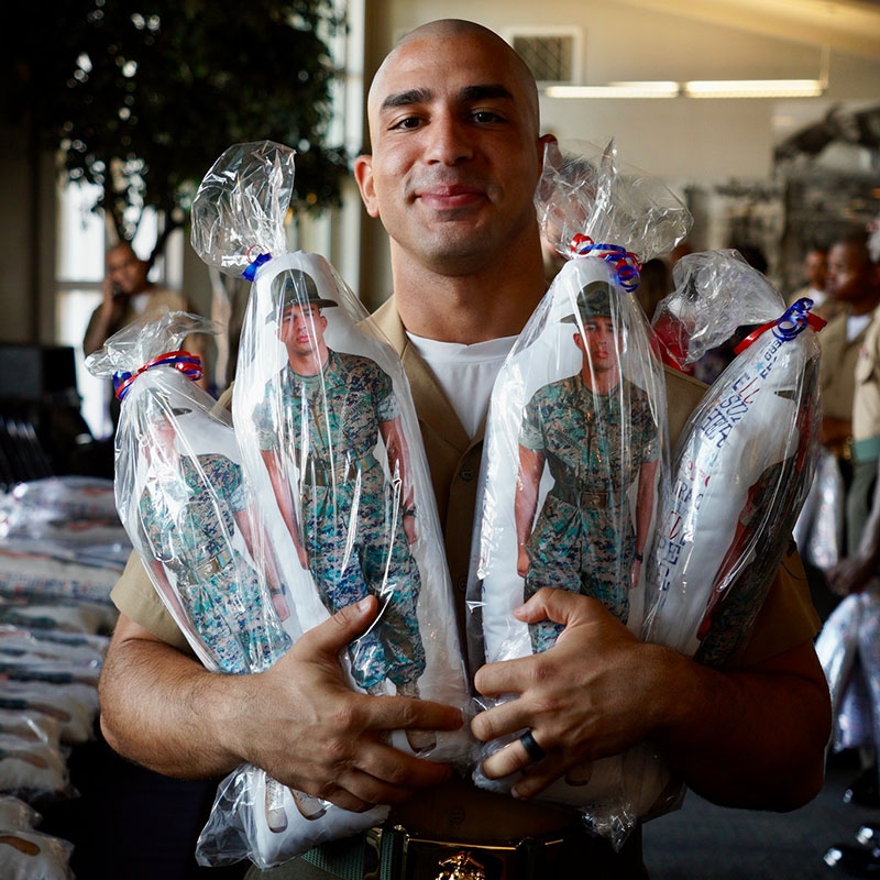 Military member holding four packaged Hug-A-Hero dolls.