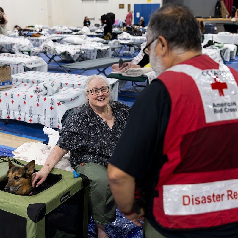 Red Cross volunteer speaking with a woman with her dog in a Red Cross shelter.