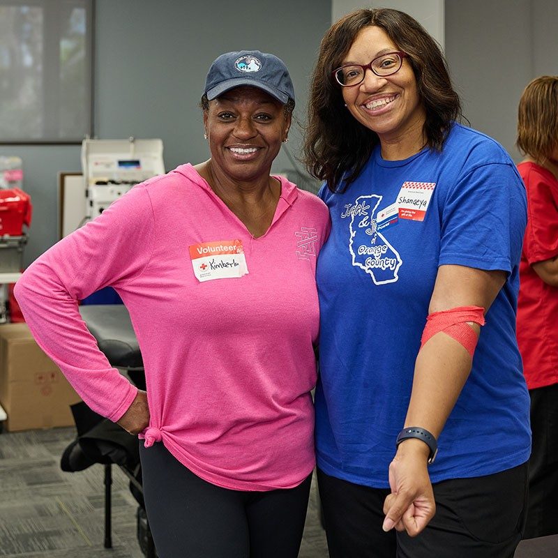 two women standing next to each other with one showing the bandage on her arm.