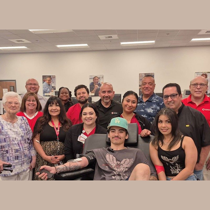 blood donor David Burton sitting in chair with Red Cross staff and other blood donors standing by him.