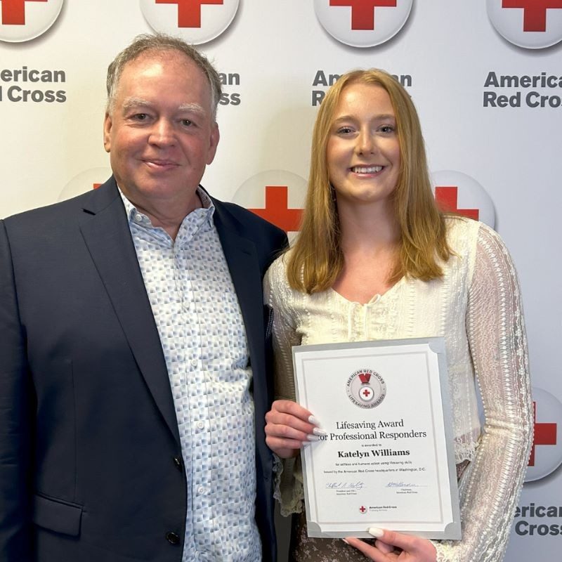 Katelyn smiling holding award in her hand next to a man.
